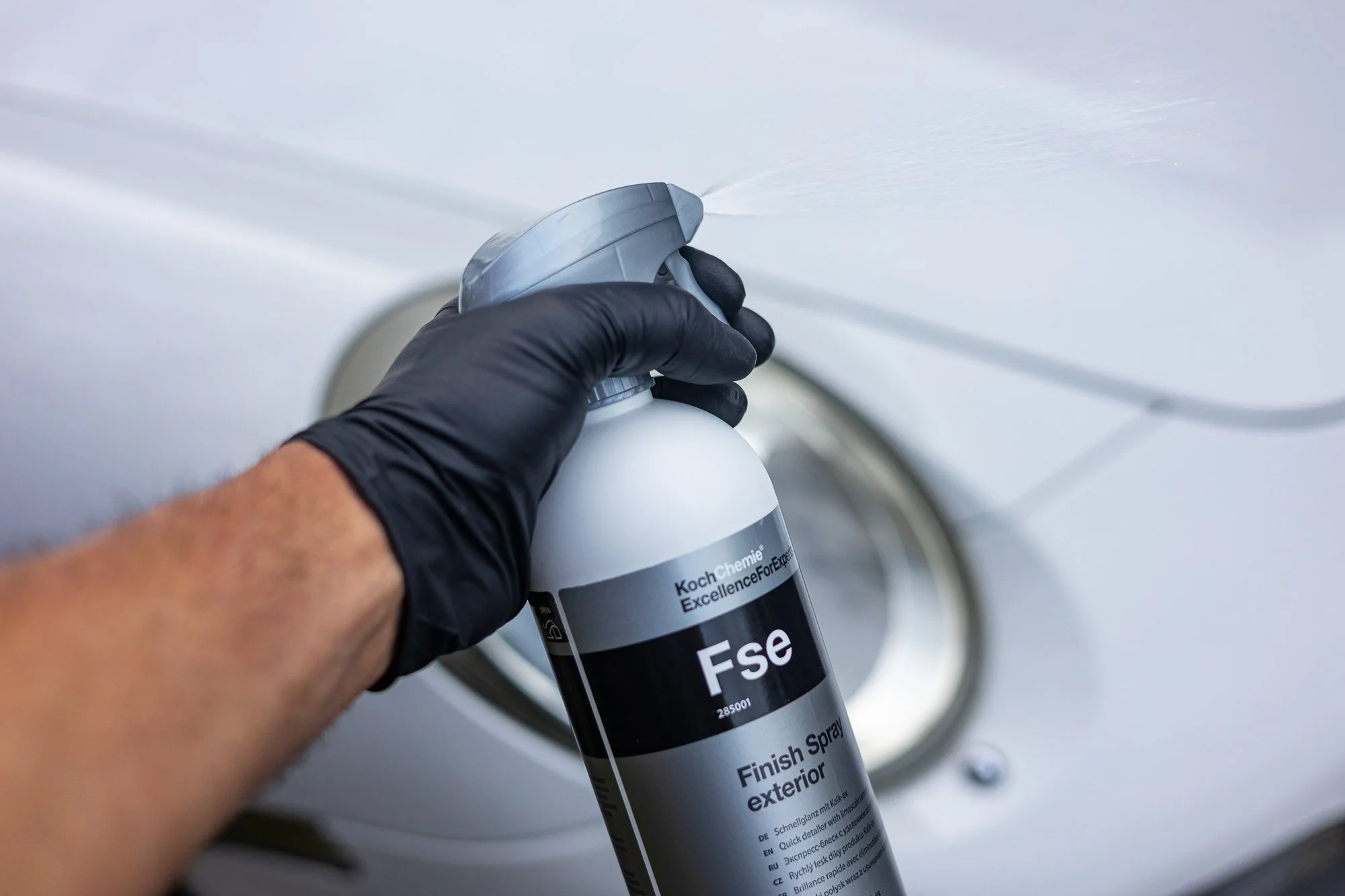 Person wearing black gloves spraying white finish spray paint on a car's exterior.