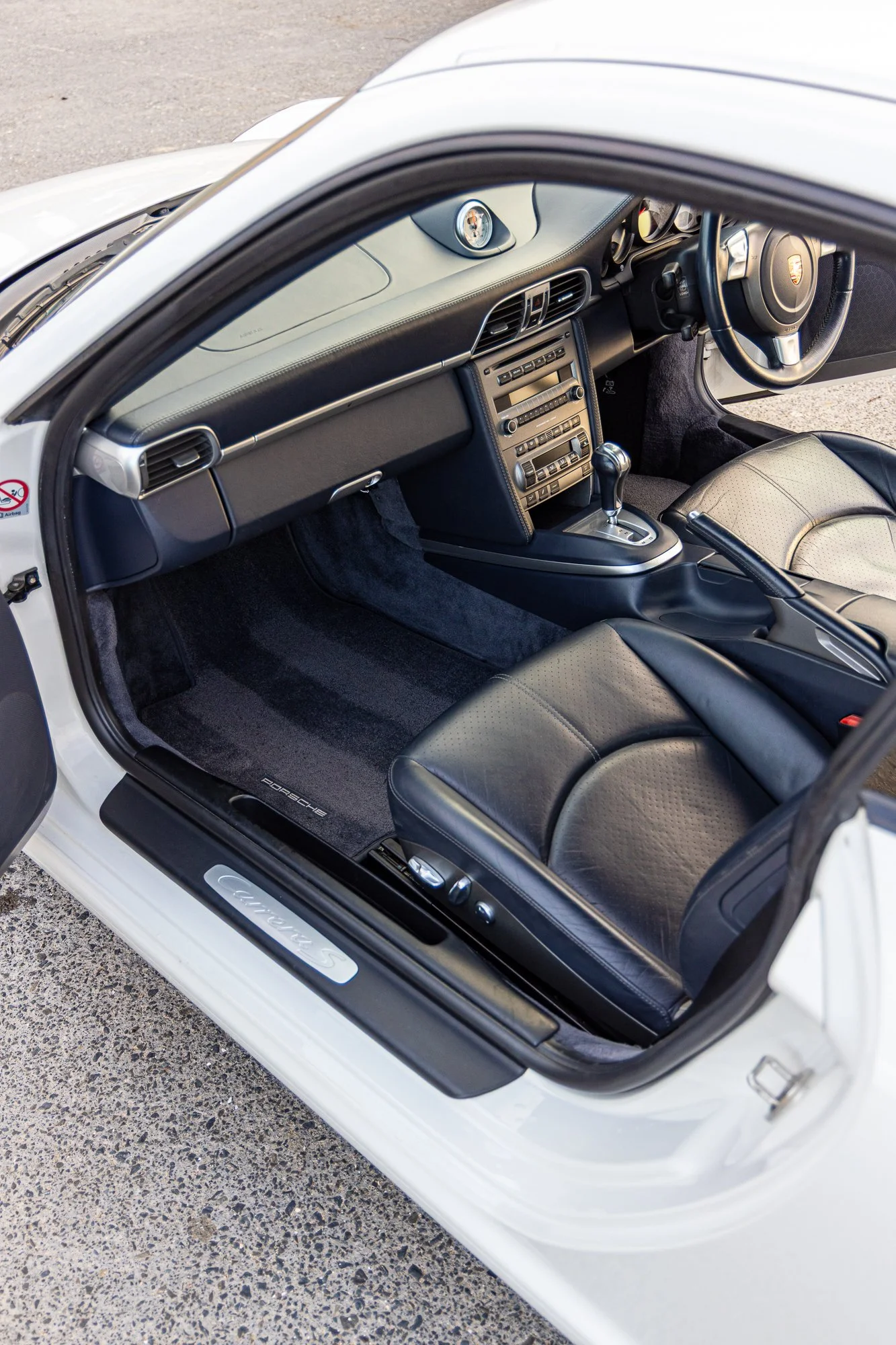 Interior of a white Porsche Carrera S sports car showing black leather seats, dashboard with central console, and steering wheel.