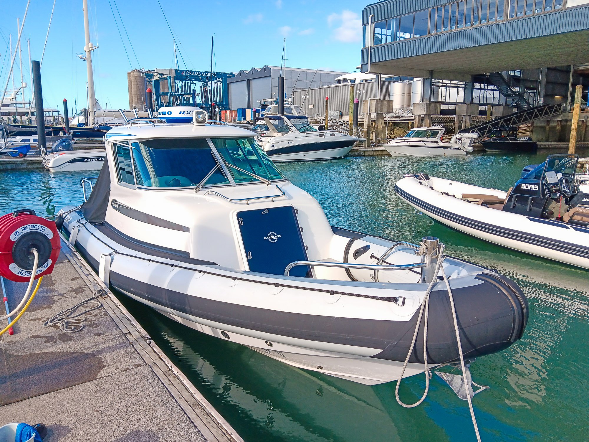 White and gray motorboat docked at a marina, with multiple boats and yachts in the background.