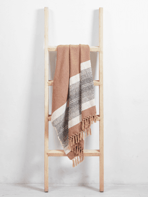 A wooden ladder with a blanket draped over one of the rungs, set against a plain white wall.