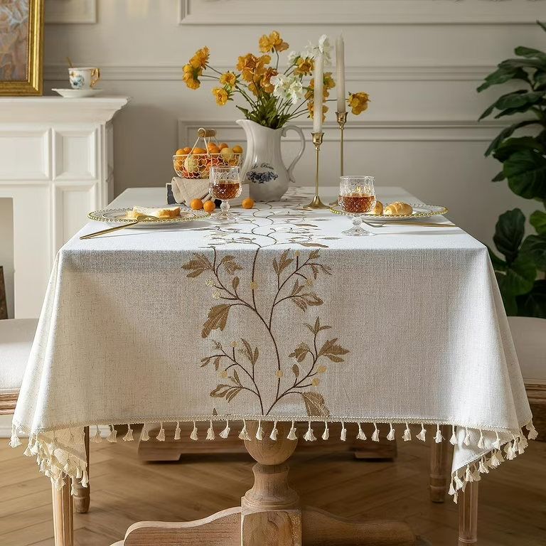 A dining table set with a floral tablecloth, flowers in a vase, glasses of tea, bread rolls, and a golden candelabra.