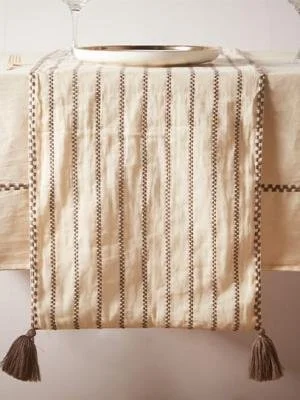 A beige tablecloth with a vertical striped pattern and fringed tassels at the corners draped over a table, with a silver tray on top.