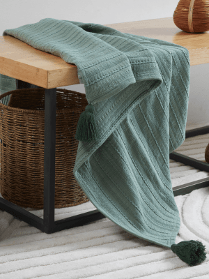 A teal knitted blanket with tassels draped over the edge of a wooden table.