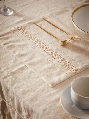 A table setting with a beige cloth, gold fork and knife, a white plate with a gold rim, and a white cup on a saucer.