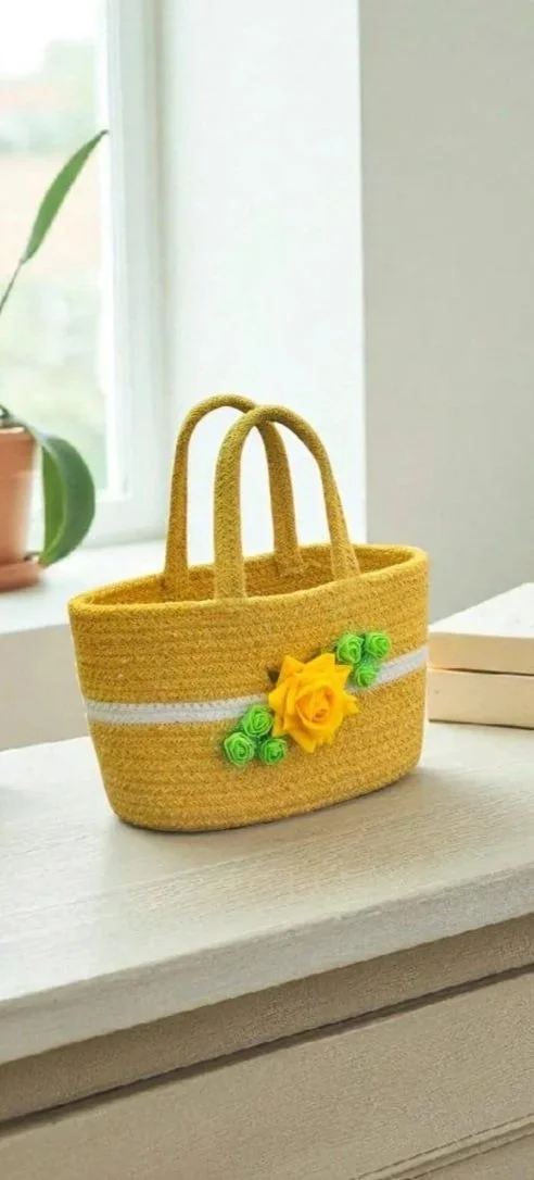 Yellow woven tote bag with green and yellow fabric flower accents on a white surface near a window.