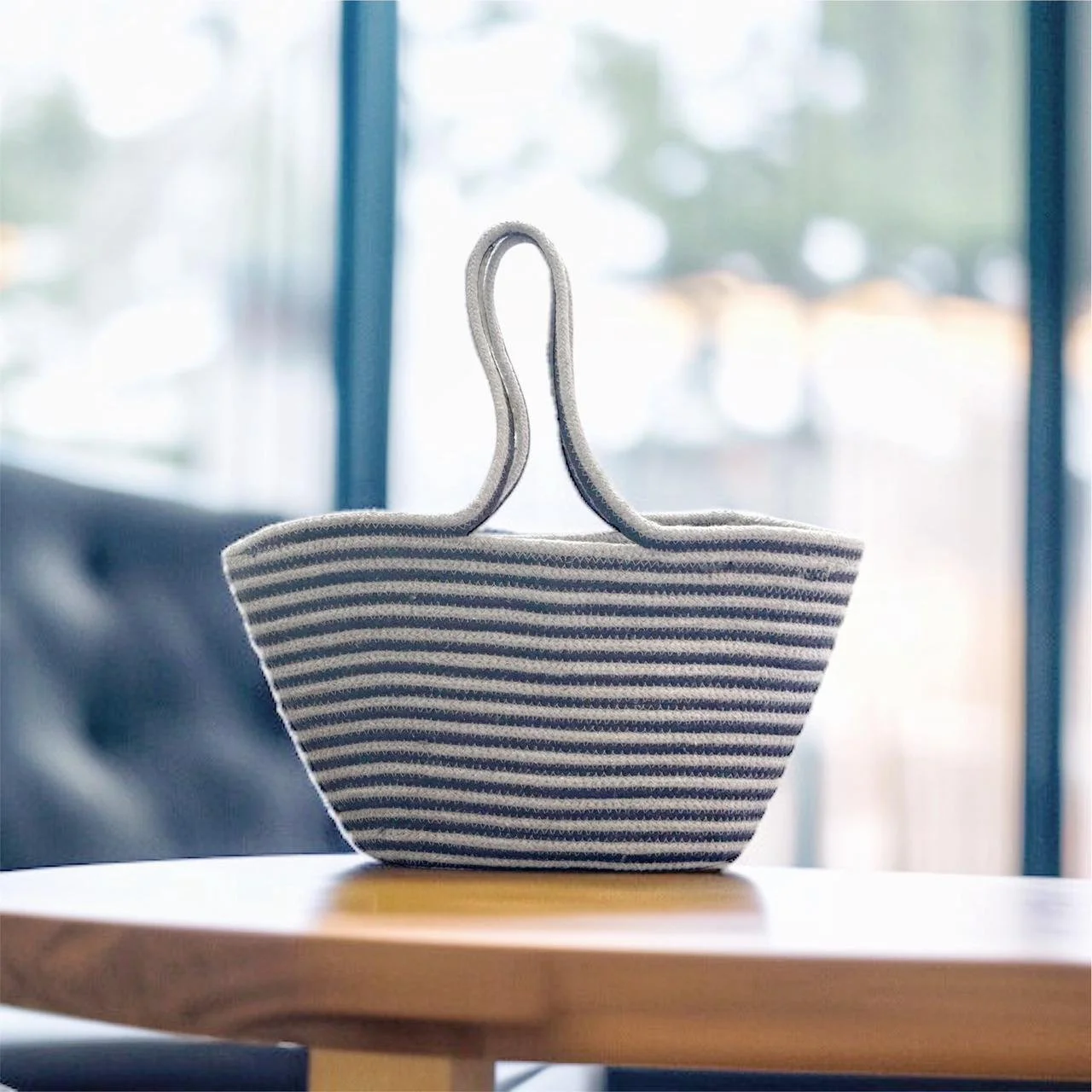 A striped fabric tissue holder on a wooden table in front of a window with blue framing.
