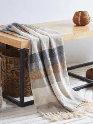 A striped blanket draped over the edge of a wooden table, with a wicker basket underneath and a decorative wicker container on top of the table.