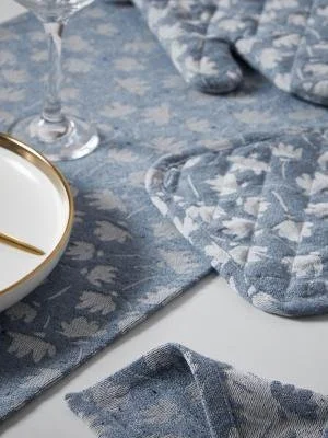 Close-up of a blue floral tablecloth, a matching oven mitt, a glass of white wine, and a small white plate with a gold fork.