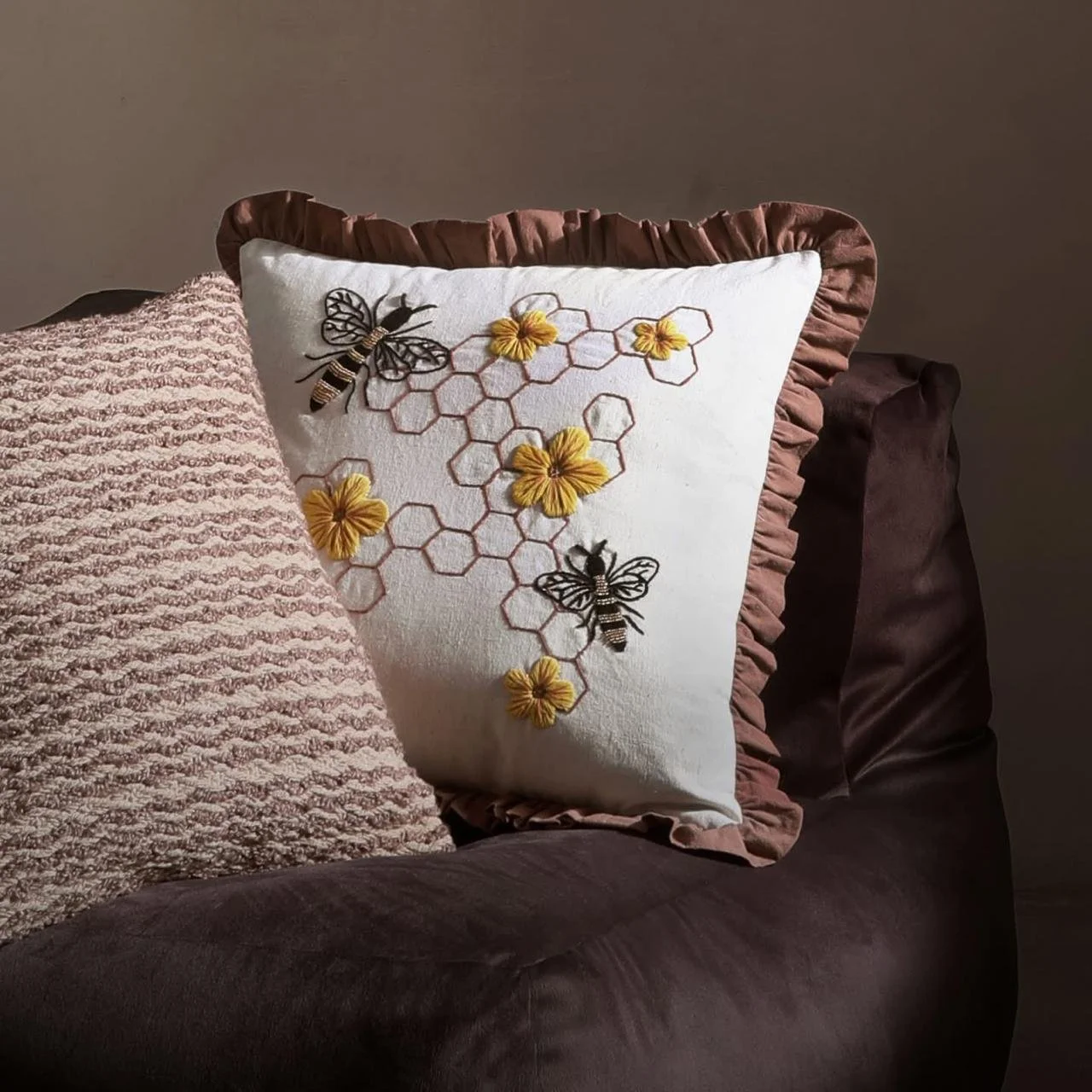 Decorative throw pillows on a dark brown couch, including one with embroidered bees, honeycombs, and yellow flowers.