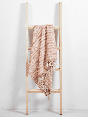 Wooden ladder with a pink and beige striped blanket hanging over one rung, against a plain white wall.