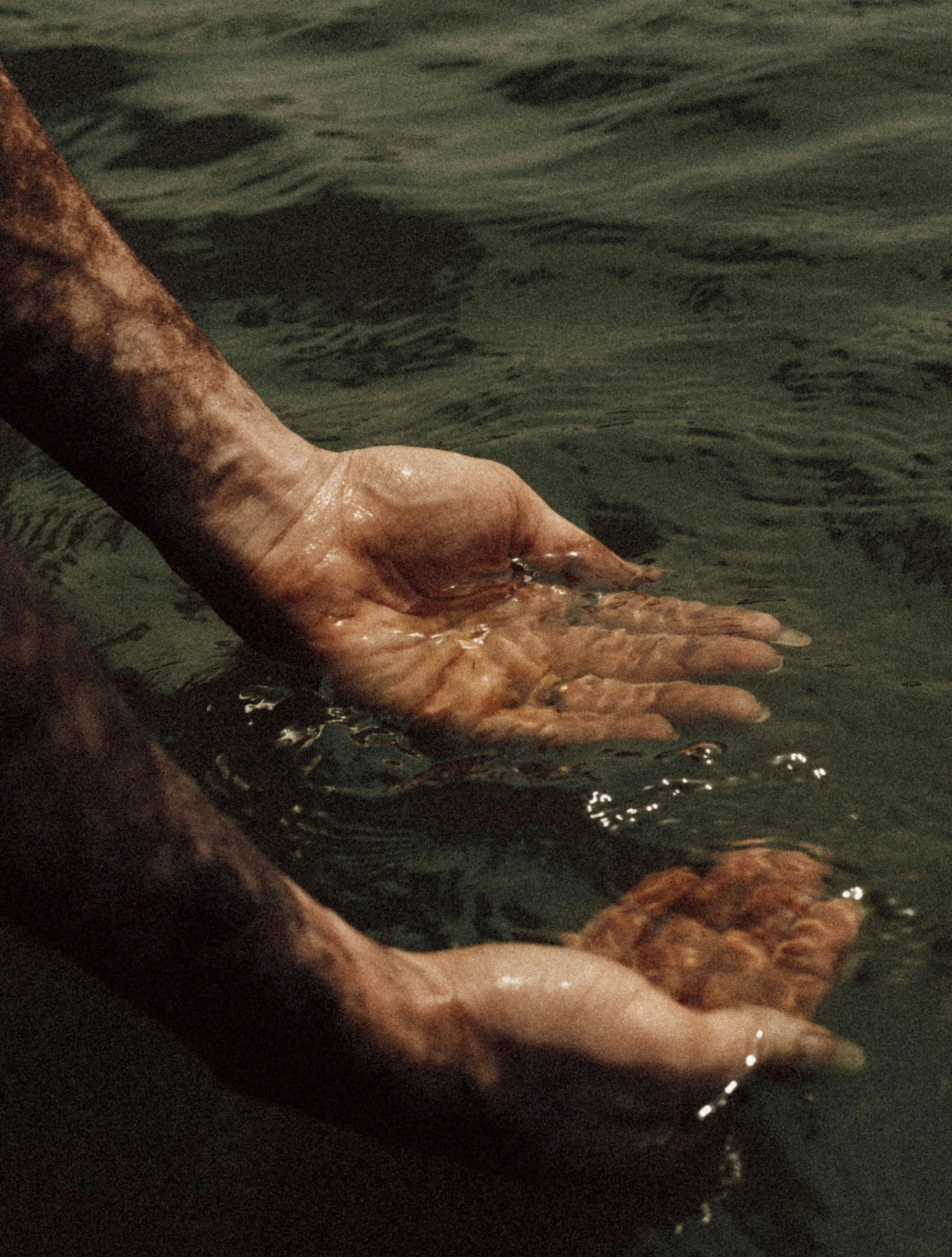 Close-up of hands submerged in water, with one hand resting on top of another.