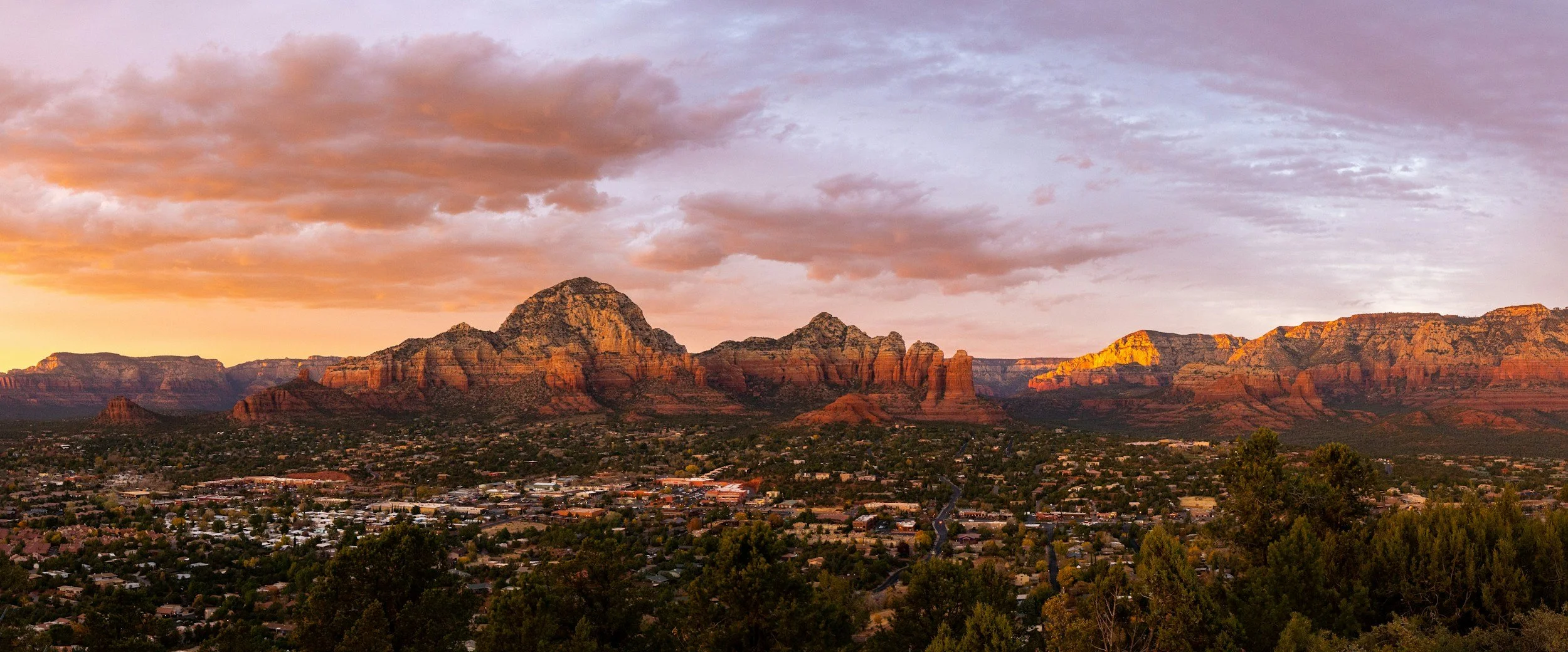Sunset over the desert landscape with red rock formations and a small town in the foreground.