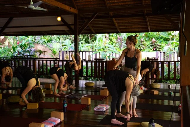 Group of women participating in a yoga class in an open-air studio with lush greenery outside.