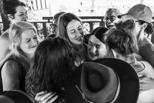Group of women in a close embrace, smiling and sharing a joyful moment outdoors.