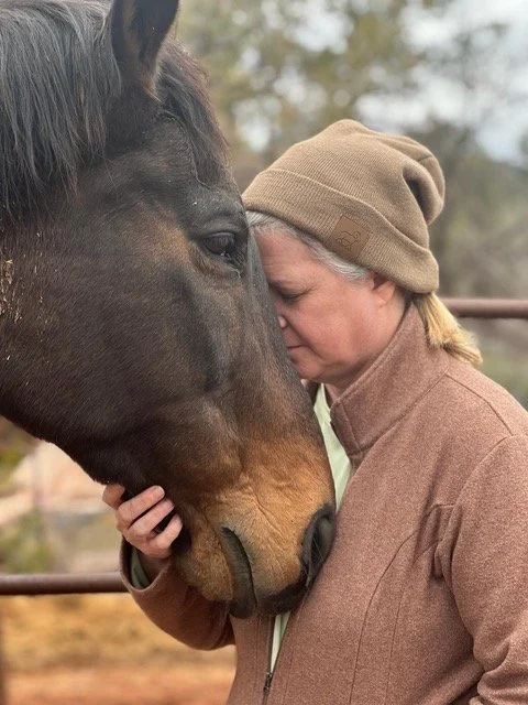 A woman with a beanie hat and brown jacket touching foreheads with a large brown horse.