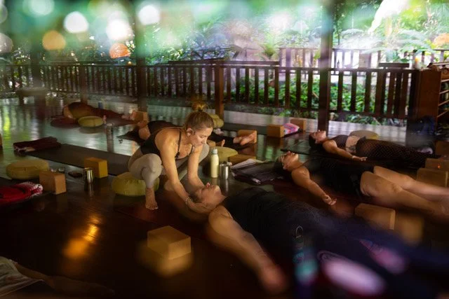 People participating in a massage or relaxation class on mats with blocks and cushions outdoors