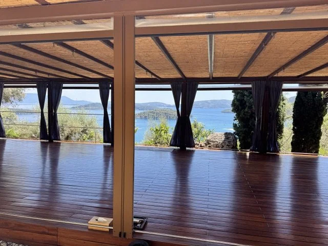 Indoor space with a wooden floor and large windows with black curtains, showing a scenic view of a lake and hills outside.
