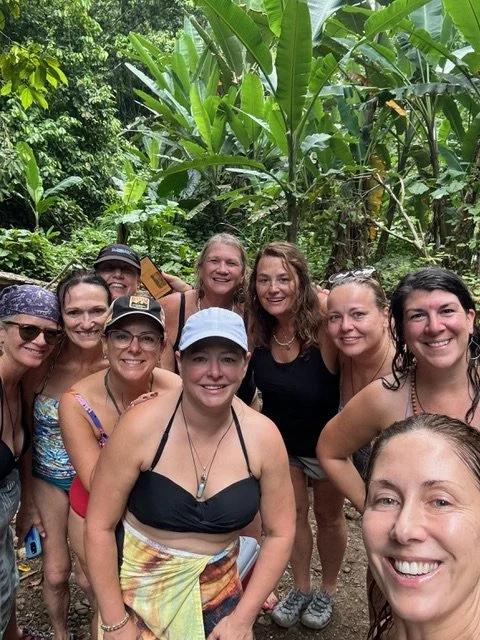 Group of women smiling in a lush jungle with large green leaves.