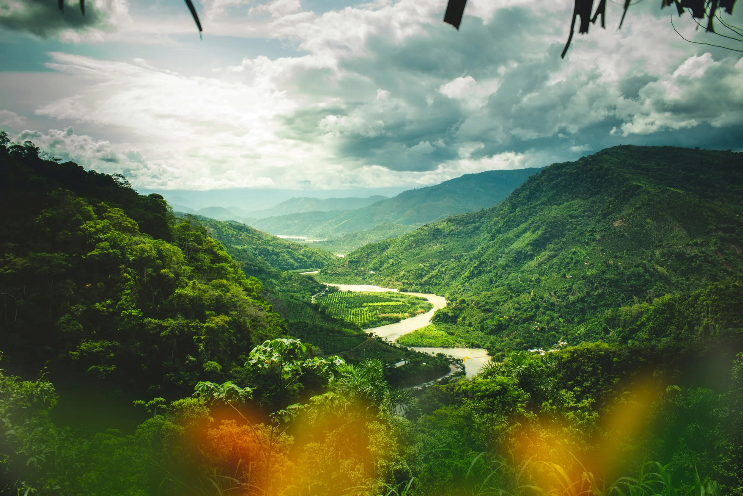Lush green mountains and a winding river under a cloudy sky.