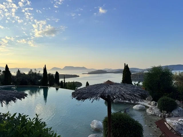 Scenic view of a pool and lake at sunset with umbrellas, trees, and distant mountains