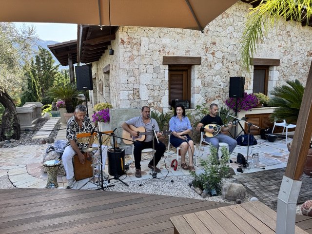 Musicians performing outdoors in a rustic setting with stone walls, potted plants, and umbrellas.
