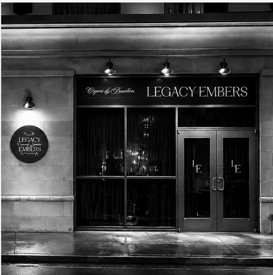 Exterior of a restaurant named 'Legacy Embers' with black signage, glass doors, and lighting fixtures above the entrance.