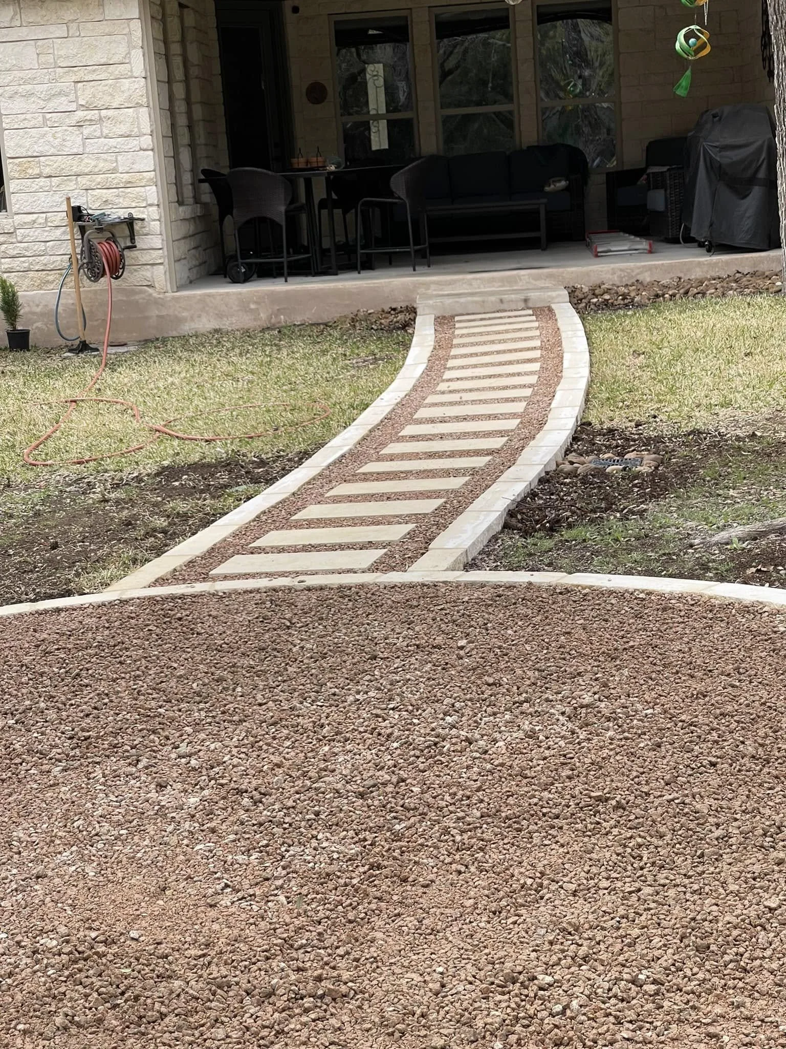 A winding stone and gravel pathway leading to the porch of a house with outdoor furniture and a grill.