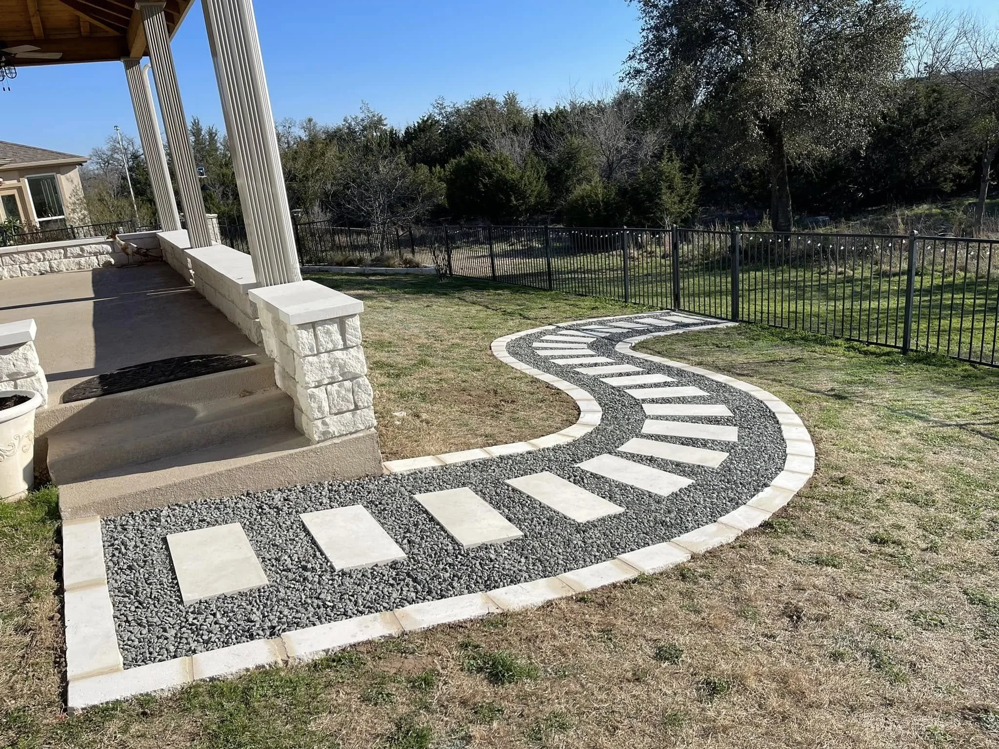 Curved stone pathway with light-colored rectangular pavers and dark gravel sections leading from a porch with white stone pillars.