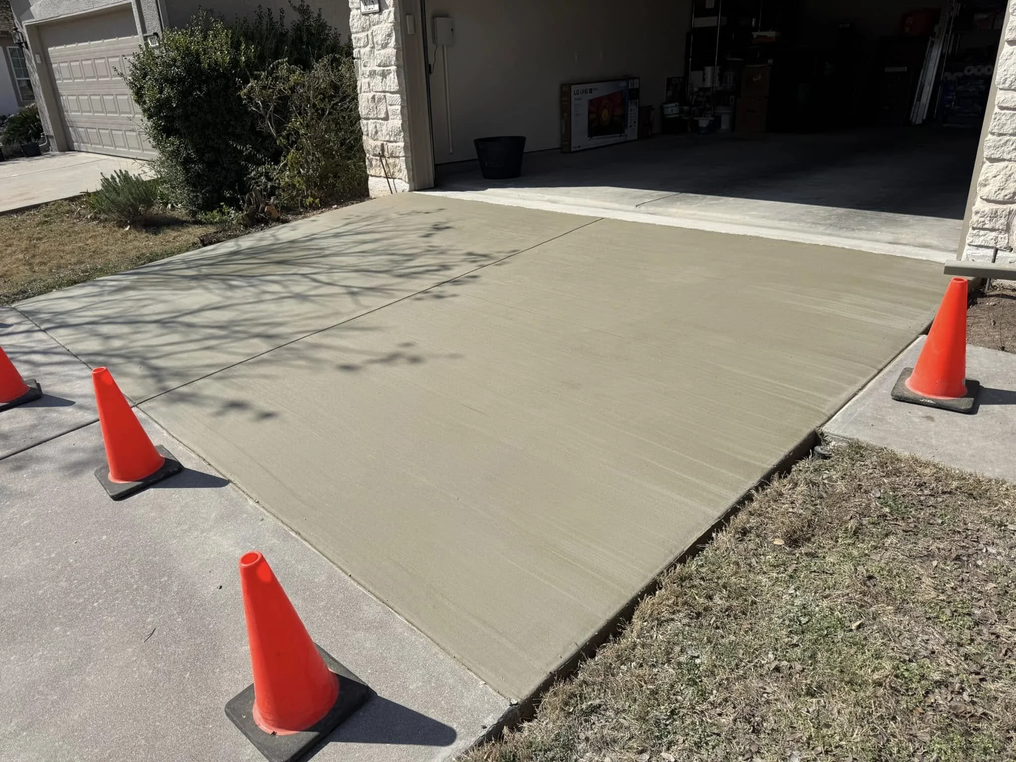 Freshly poured concrete driveway with three orange traffic cones marking the area in front of a garage.