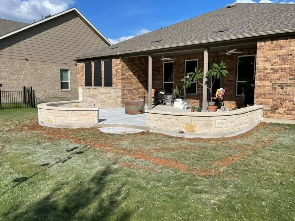 Backyard patio with a curved stone wall, potted plants, and outdoor furniture, attached to a brick house with a screened porch.