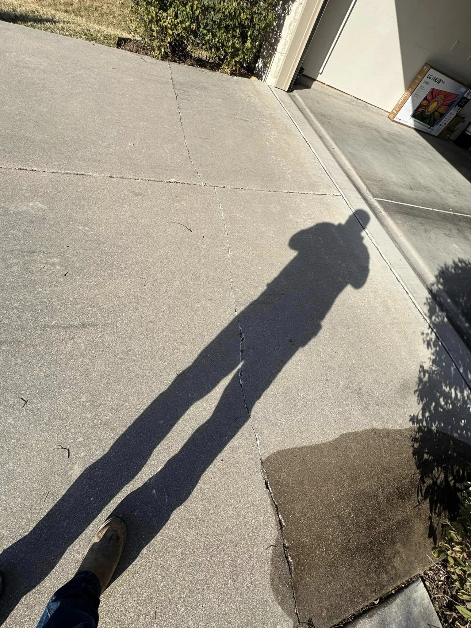 Shadow of a person taking a photo on a concrete driveway in front of an open garage door, with a box on the floor inside the garage.