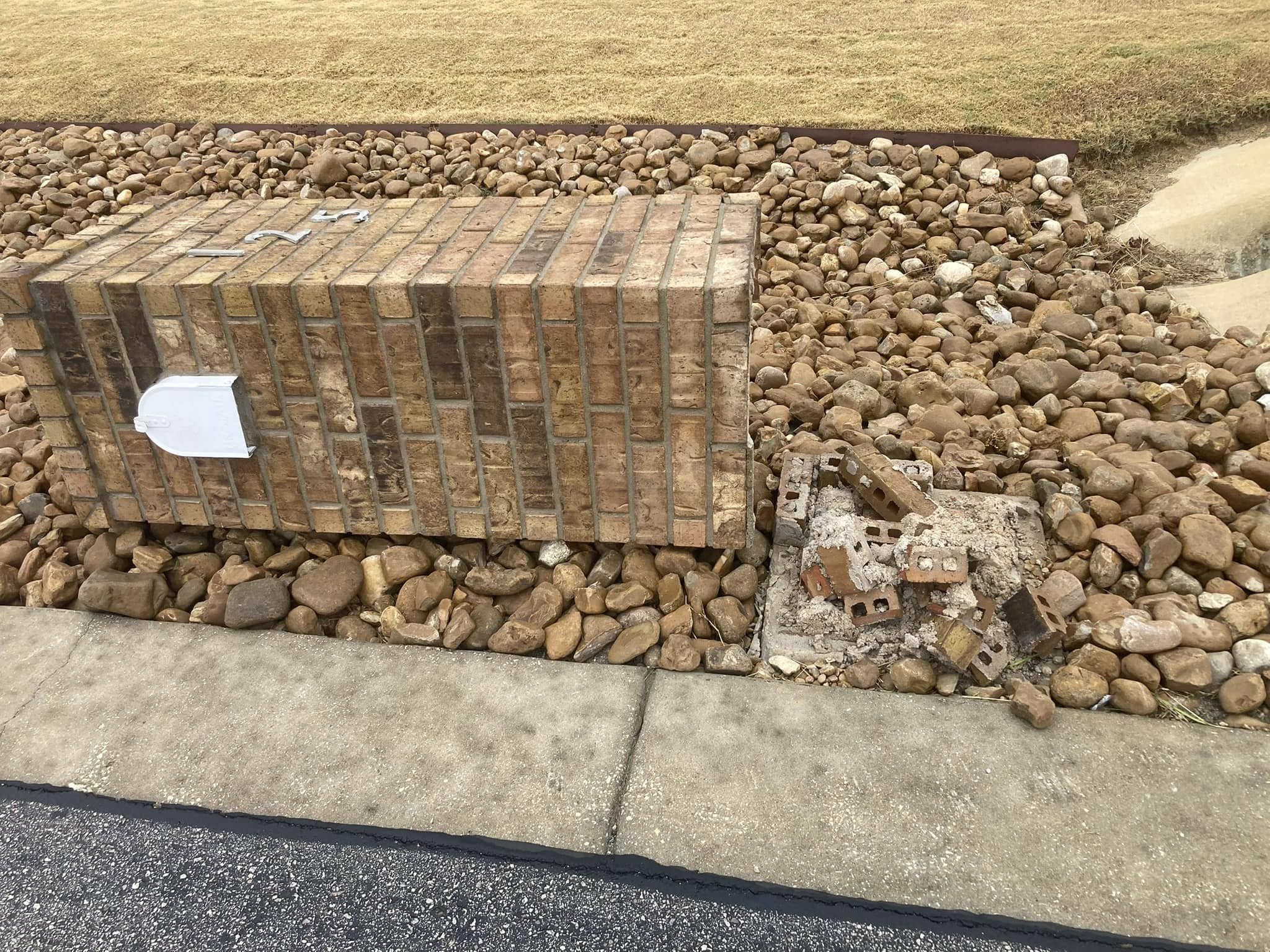 Brick mailbox on a landscaped rock bed with a pile of broken bricks beside it.