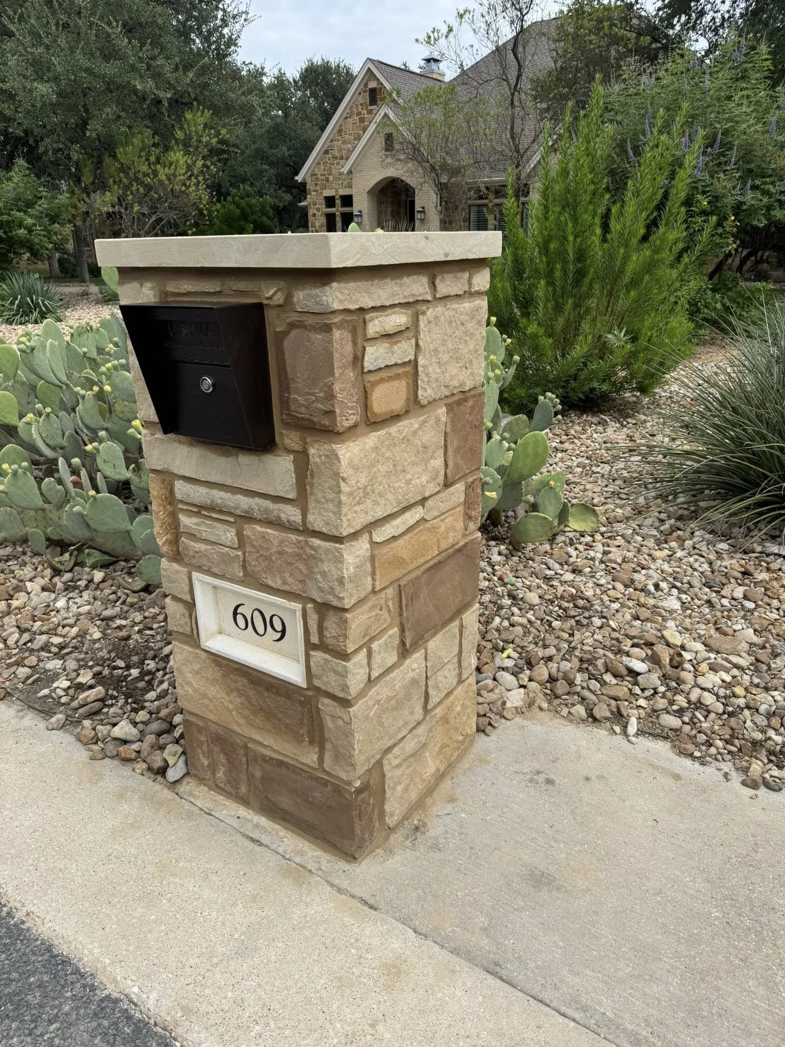 Stone mailbox with House Number 609 in front yard of a house with desert landscaping and cacti.