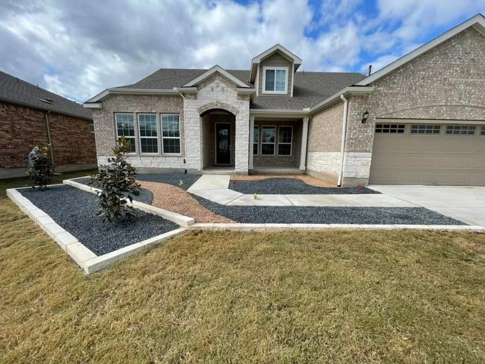 Front yard of a new house with a landscaped garden, walkway, and driveway under a partly cloudy sky.
