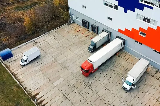 Four delivery trucks parked in front of a large warehouse or commercial building.