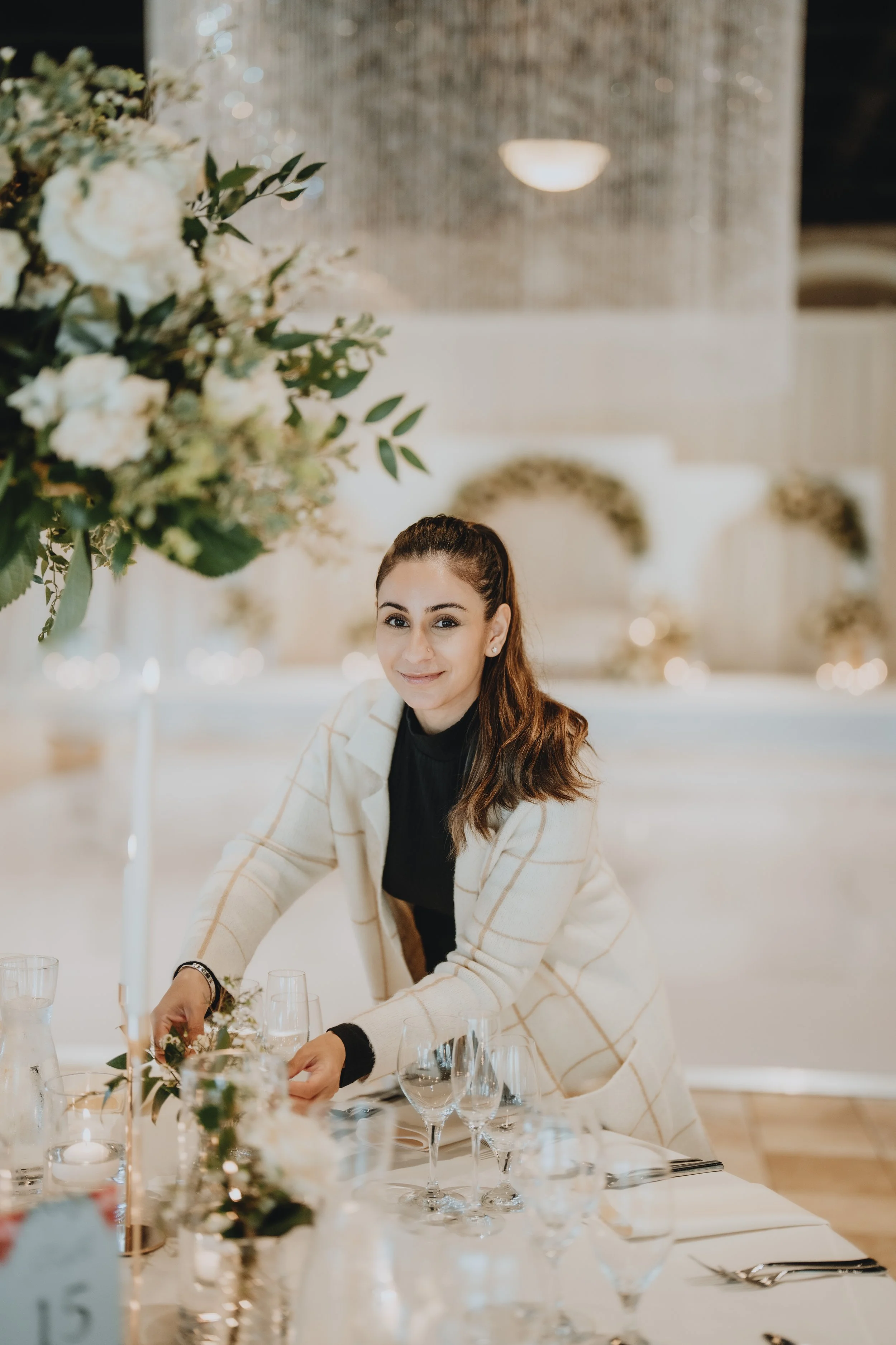 A woman arranging table settings at an elegant event with floral centerpieces and glassware.