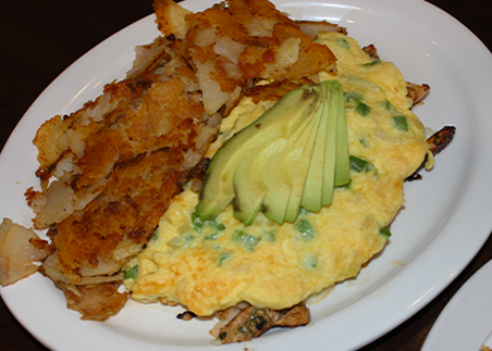 Omelette with avocado slices and hash browns on a white plate
