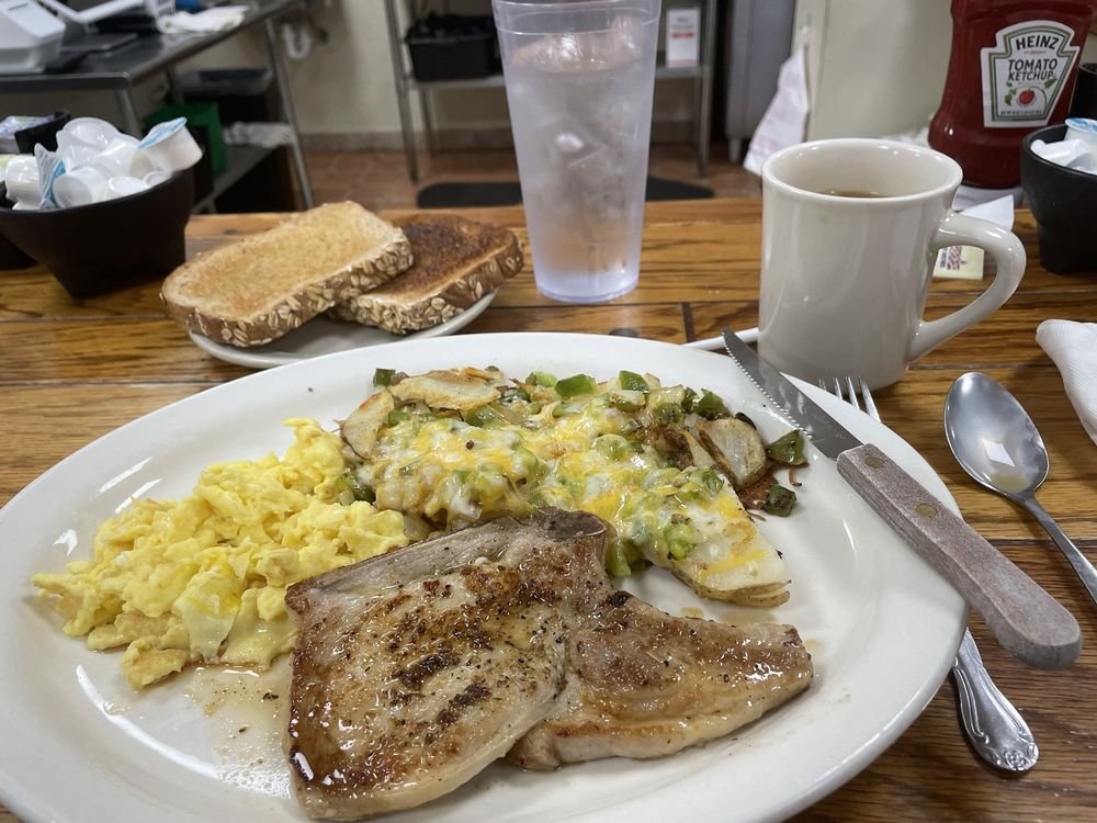 Breakfast plate with scrambled eggs, cheesy potatoes, and grilled chicken. In the background, toast, a glass of iced water, a cup of coffee, and condiments.