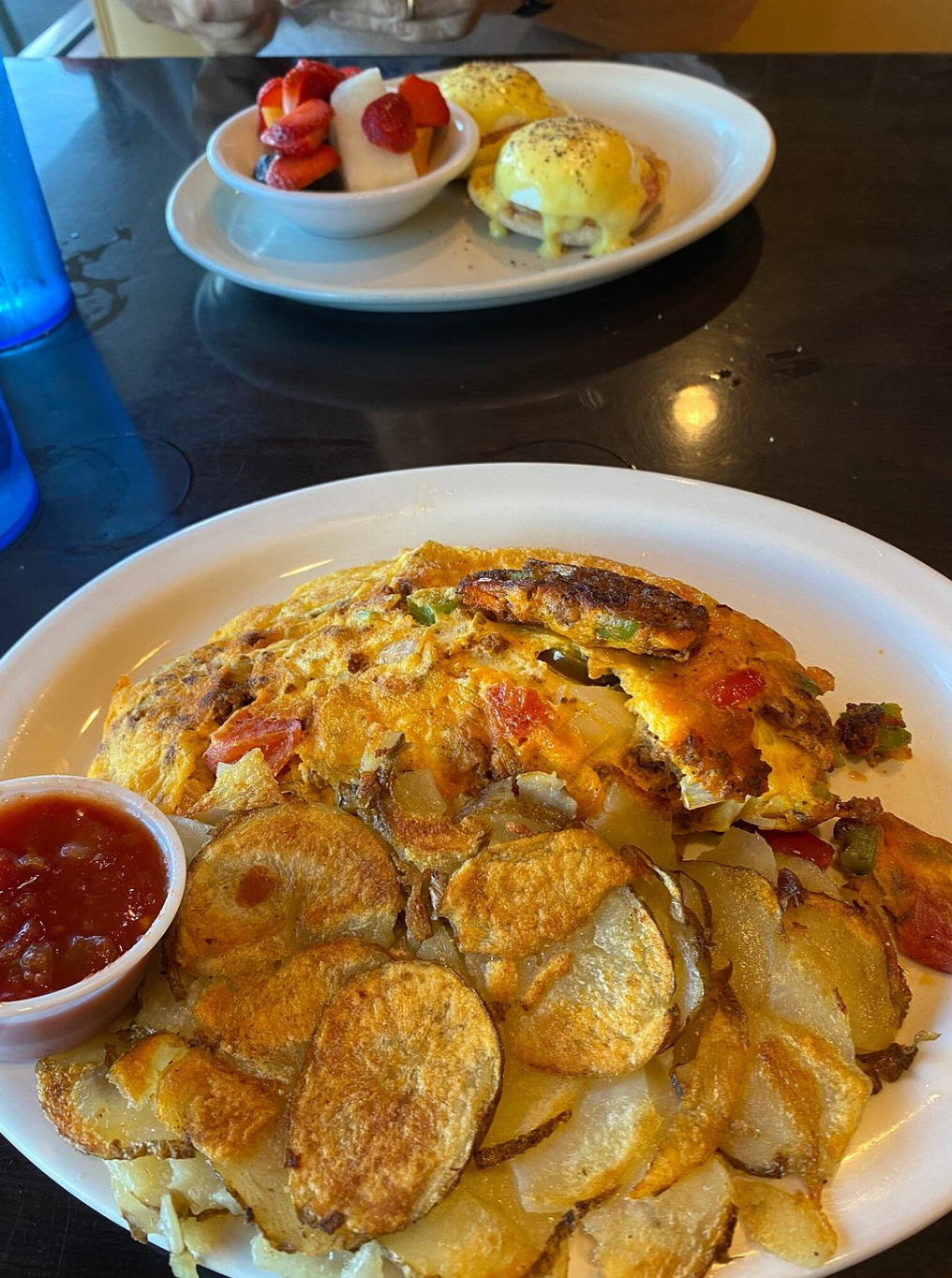Plate of breakfast food with eggs and potatoes, and a bowl of strawberries with whipped cream in the background.