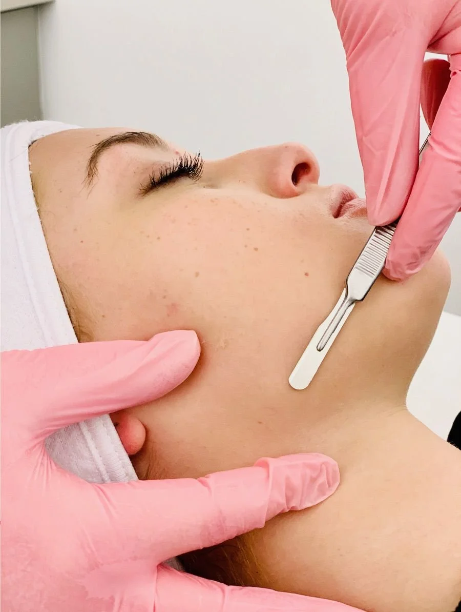 Esthetician wearing pink gloves giving client dermaplane treatment