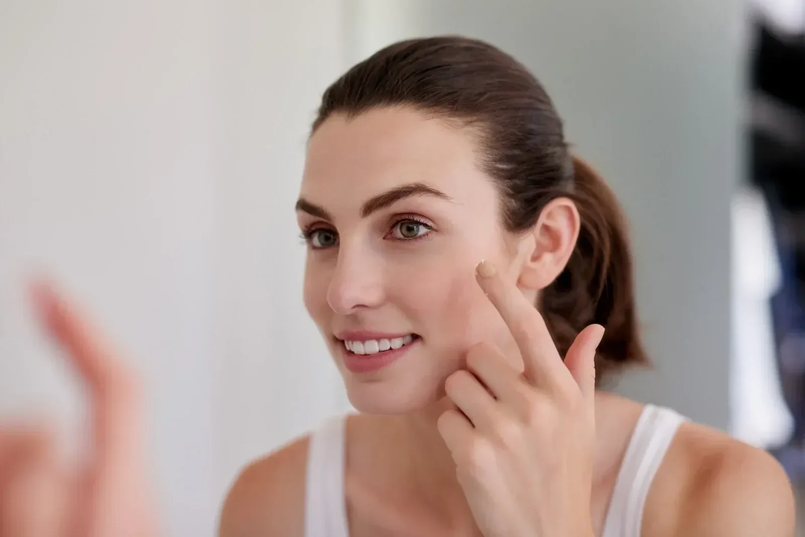 woman looking in mirror applying skincare to her face