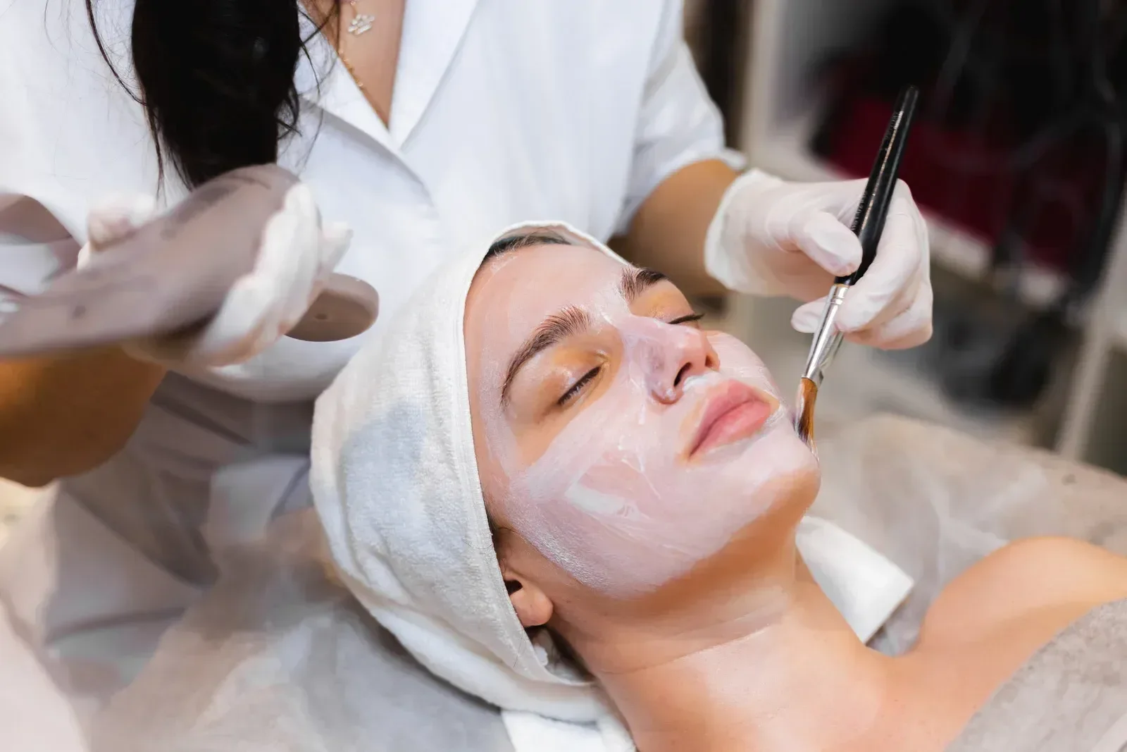 Woman with eyes closed receiving facial with brush in a spa like setting