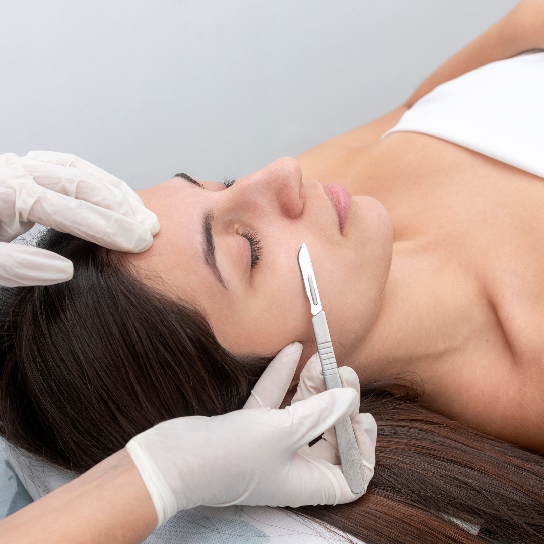 woman receiving dermaplane treatment by esthetician wearing white gloves holding a scalpel