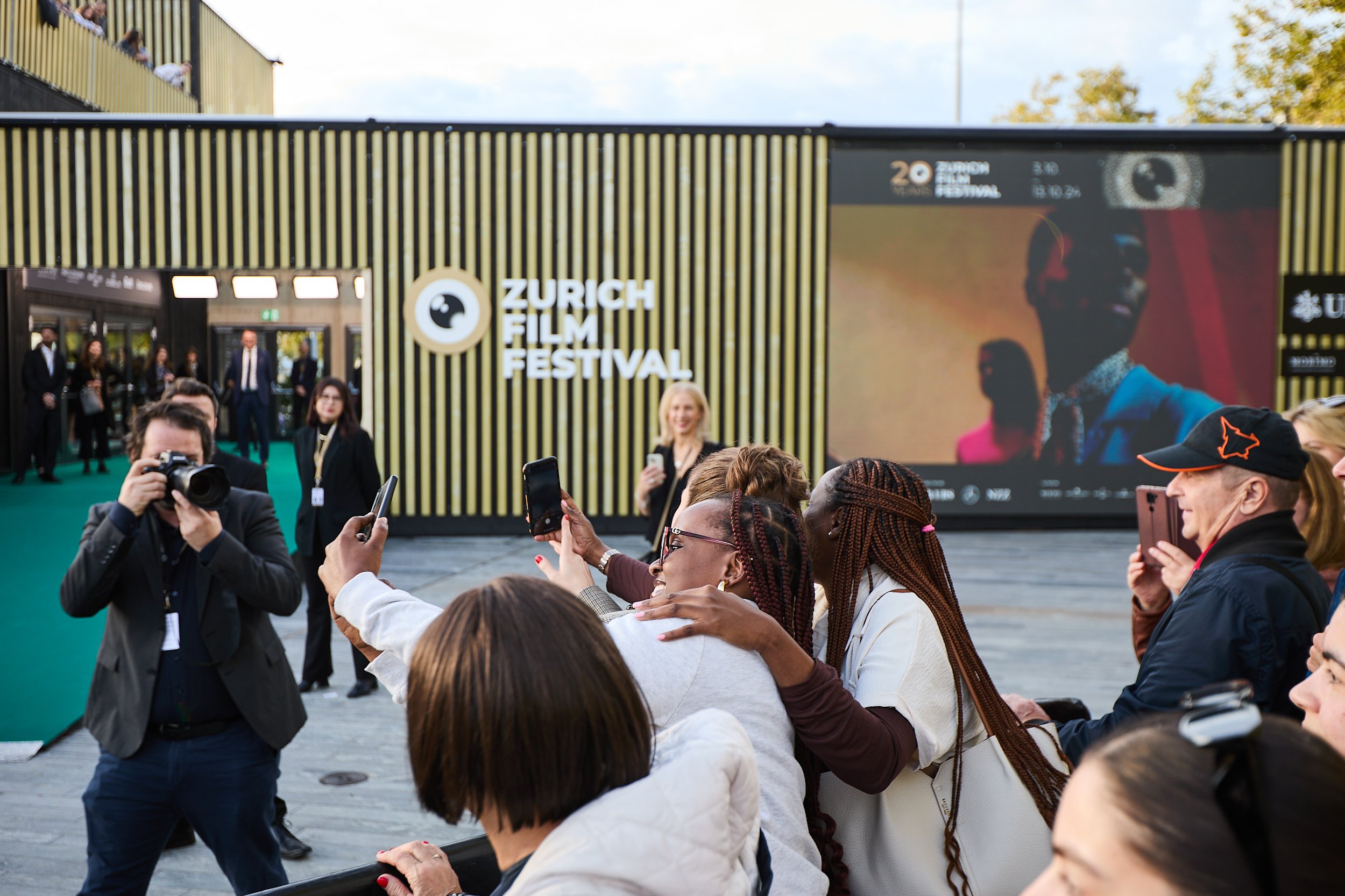 People taking photos at Zurich Film Festival entrance with a large display screen in the background.