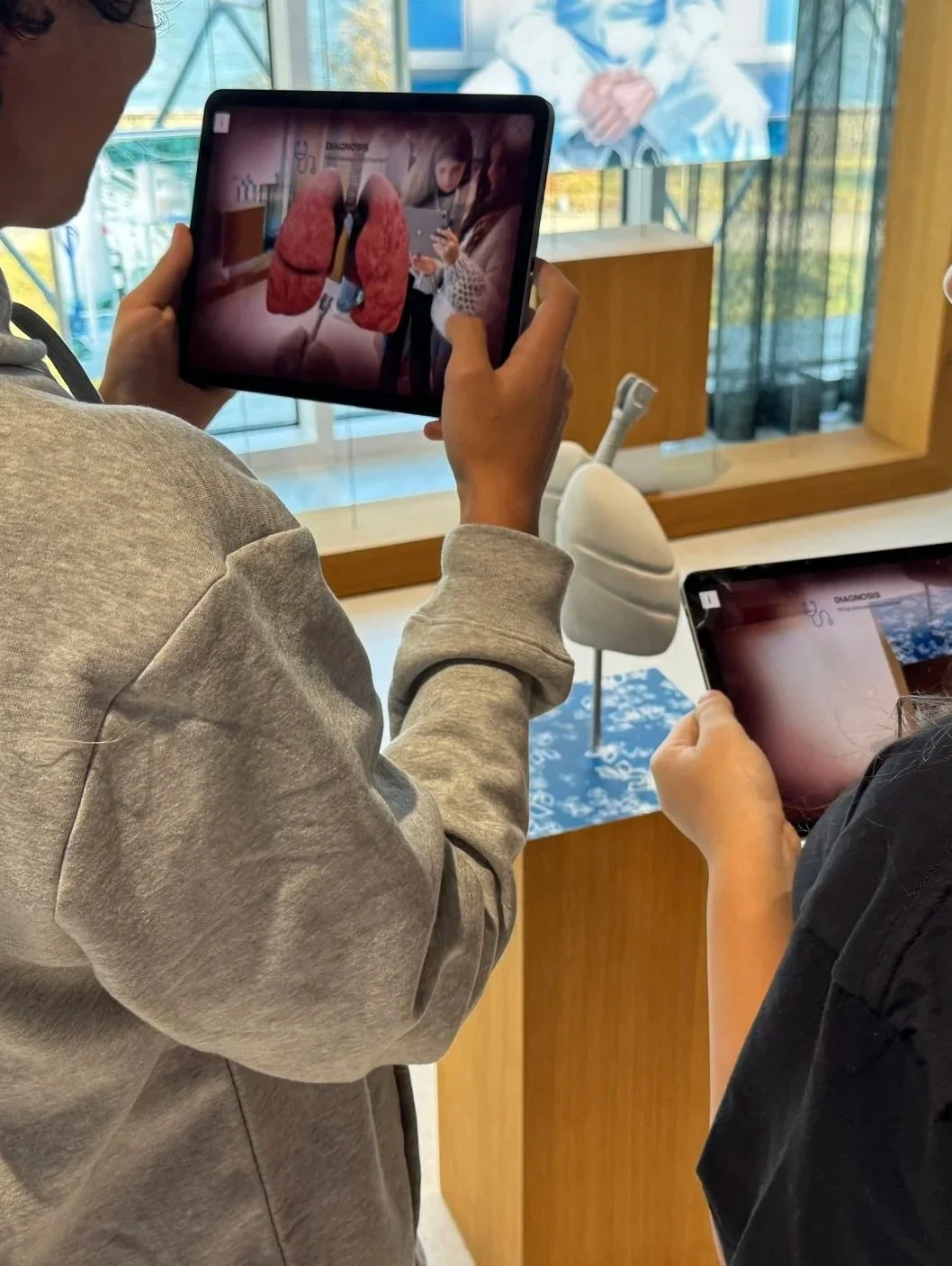 Two people are taking photos of a digital display showing lungs with a medical diagram, in a medical or educational setting.