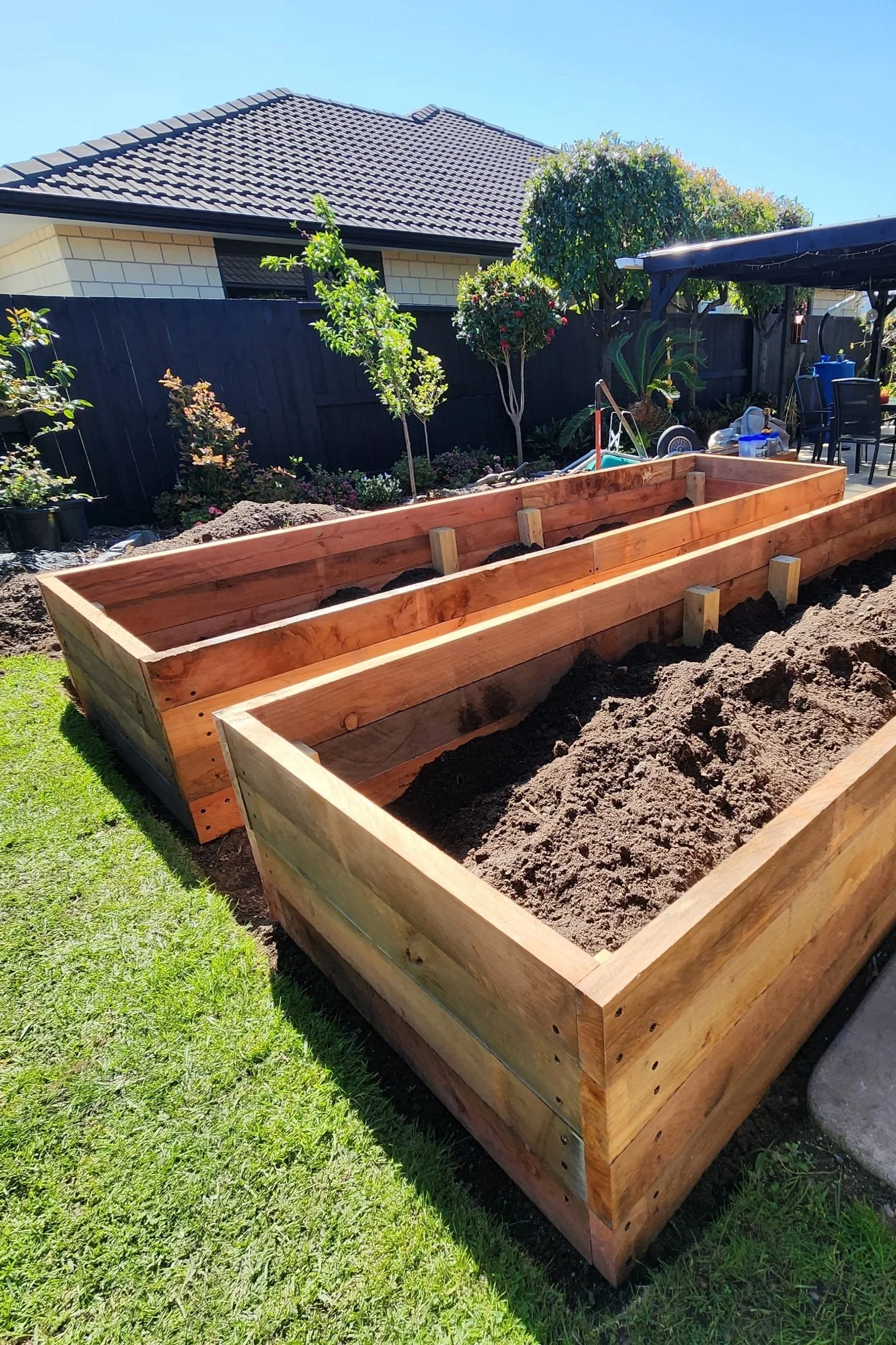 Newly built wooden garden beds filled with soil in a backyard.