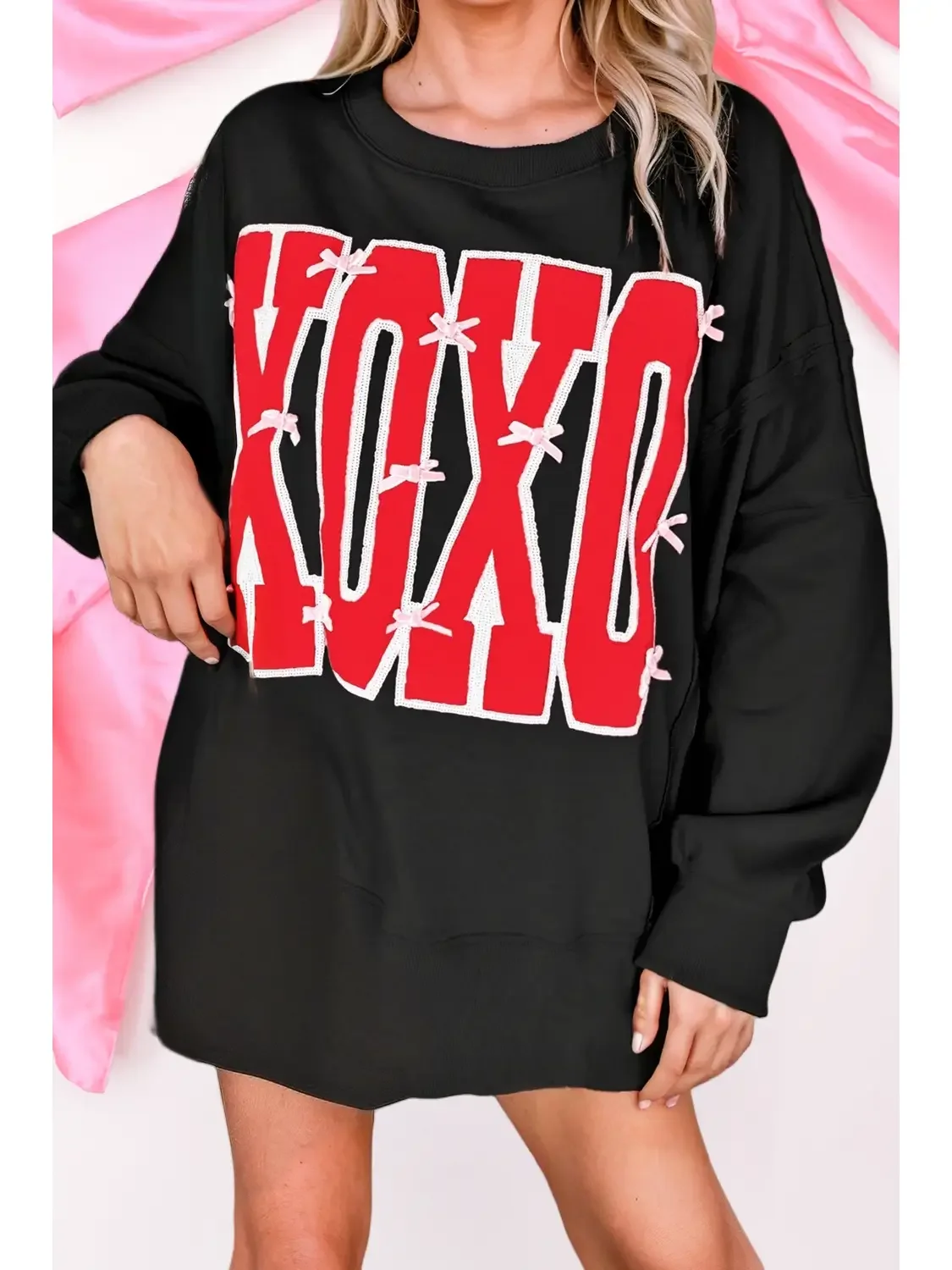 A woman wearing a black sweatshirt with red and white text that says 'LOVE,' with pink bows and a black skirt or shorts.