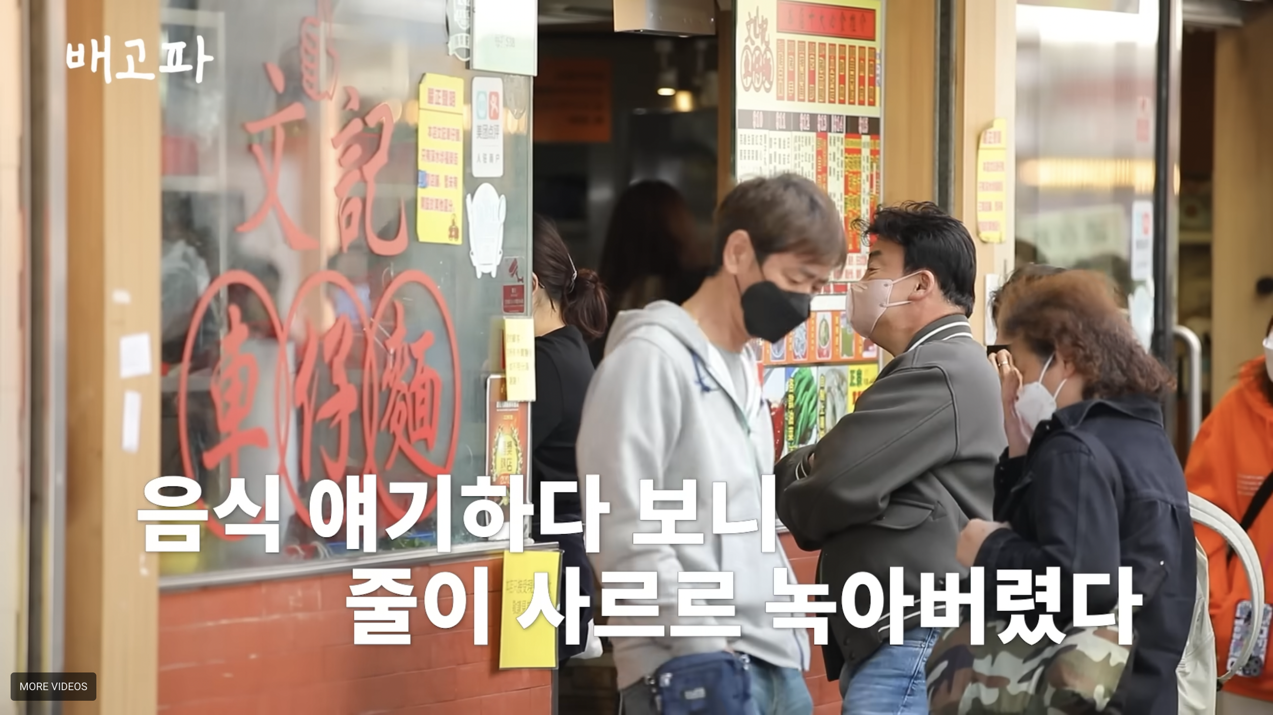 People wearing masks stand in line outside a restaurant with a glass window displaying Chinese characters and a colorful menu, waiting to order food.