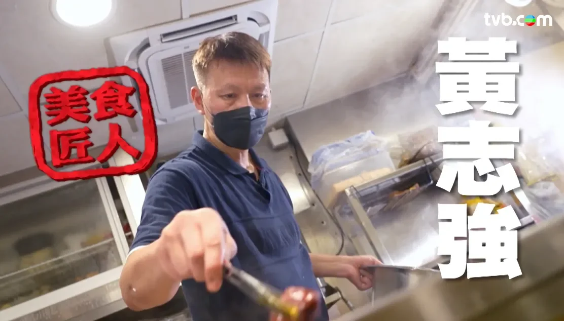 A man wearing a blue shirt and black face mask working in a kitchen with steam rising. There is Japanese text on the right and a red stamp with Japanese characters on the left.