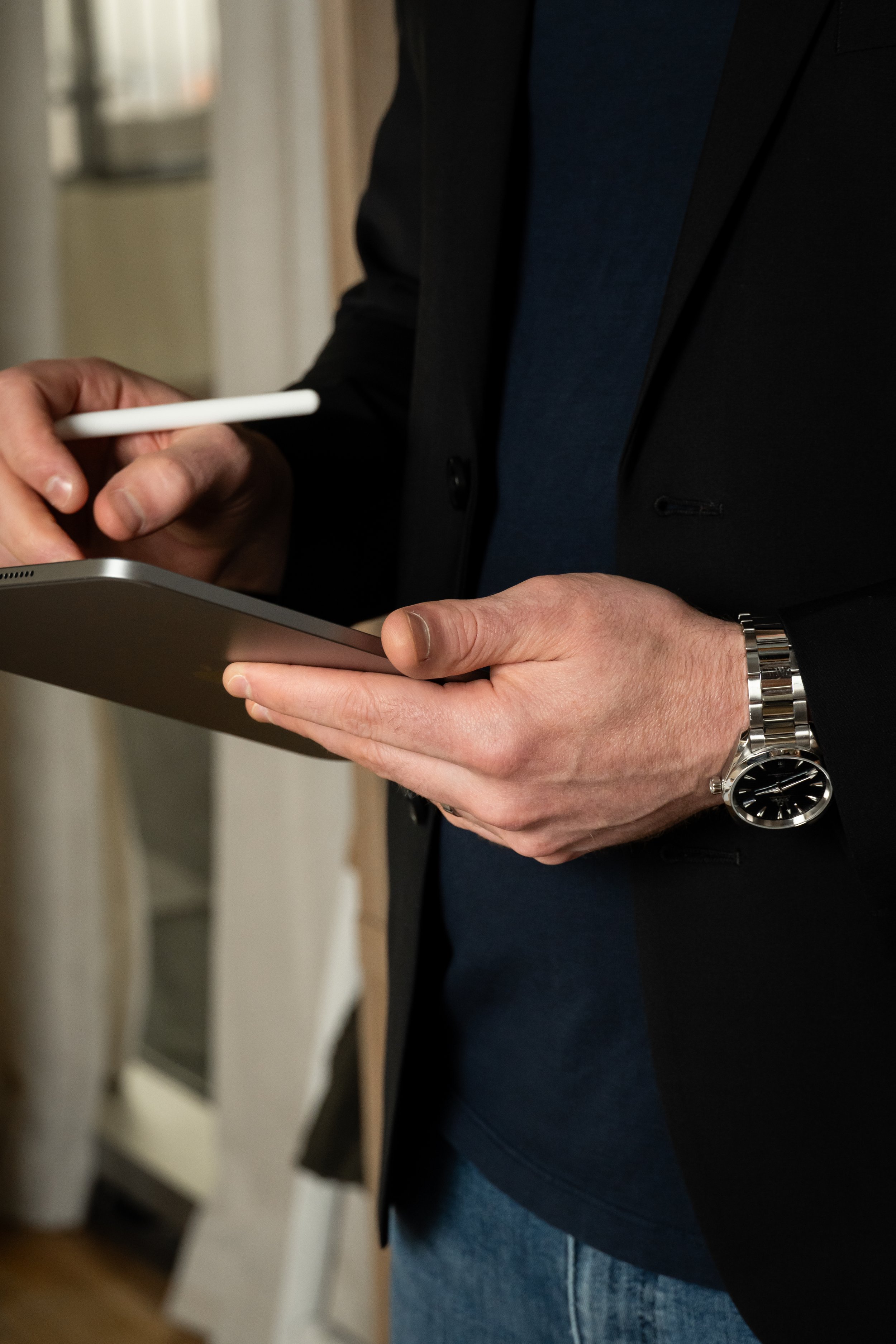 A person in a black blazer and blue shirt holding a tablet and a stylus in an indoor setting.
